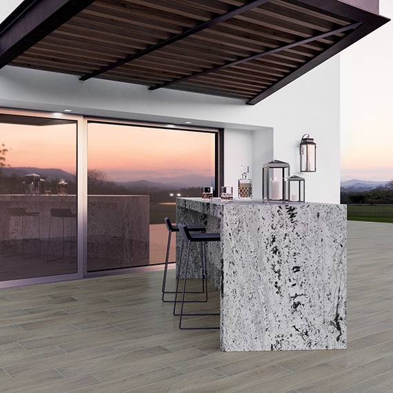 Backyard covered patio with wood look tiled floor, black and white granite waterfall bar, bar stools, wooden awning, and sliding glass door.