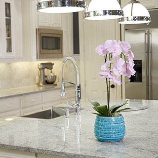 Large kitchen island with white and grey granite. Orchid in blue pot on the counter next to the sink.