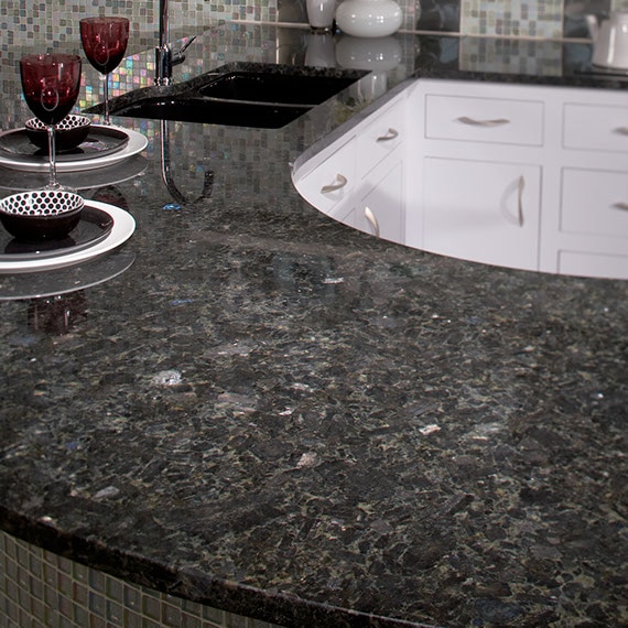 Kitchen peninsula with black, gray, and blue grained granite. Wine glasses on top of the counter.