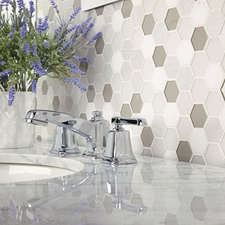 Closeup of bathroom backsplash of white, off-white, and gray stone and glass mosaic tile, marble countertop, polished silver faucet, and bouquet of lavender.