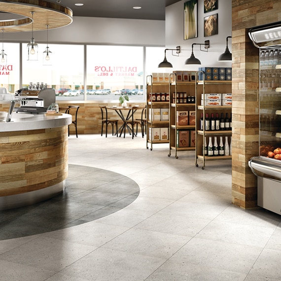 Small market and deli shop with industrial style shelving on the side containing products. Cafe tables in the background. Concrete-look porcelain tile on the floor.