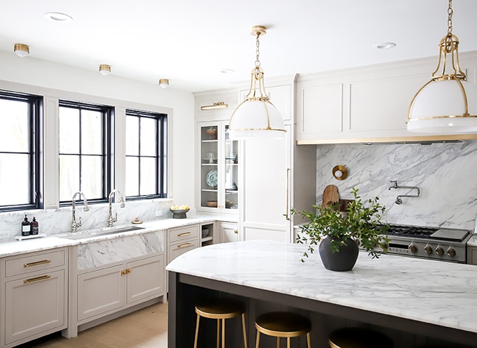 Kitchen with white cabinets. farmhouse style sink, center island, and a white marble slab countertop and backsplash.
