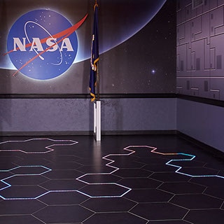 Kennedy Space Center Visitor Complex’s Astronaut Encounter Theater lobby with multi-colored neon string light intertwined throughout black hexagon floor tile.