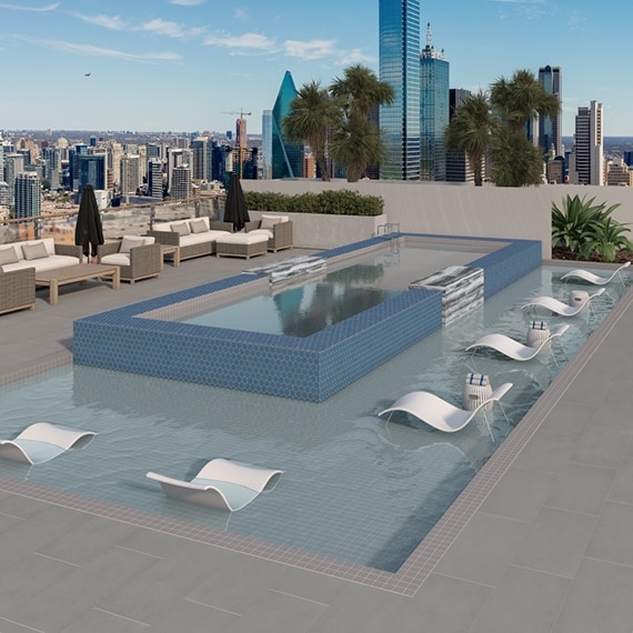 Rooftop pool with gray slip-resistance pool deck tile that looks like concrete, blue mosaic pool tile, gray mosaic tile pool border, and view of city skyline. 