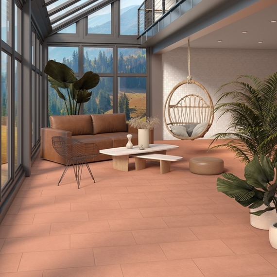 Sunroom with terracotta concrete-look tile flooring, beige mosaic wall tile, brown leather sofa, hanging rattan swing chair, picture windows showing mountain forest.
