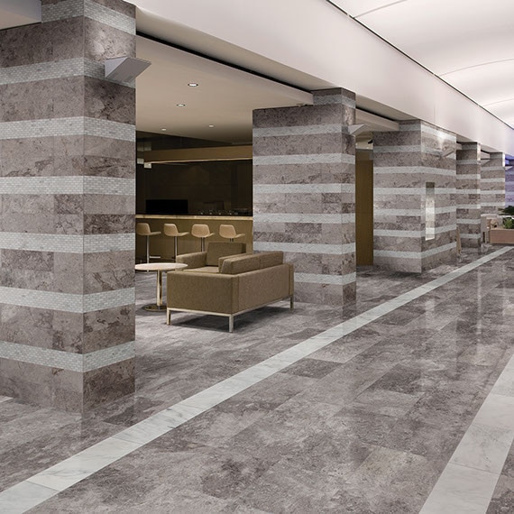 Hotel corridor with silver gray limestone on the floors, gray limestone columns with white limestone stripes, hotel bar with tan sofa & bar stools.