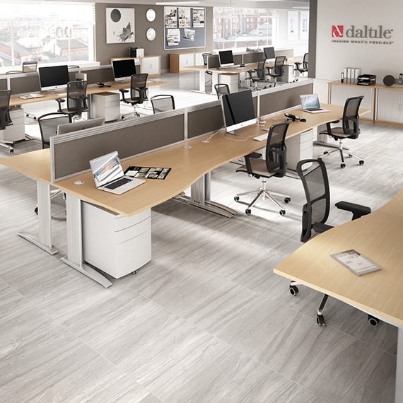 Open concept office with gray stone look floor tile, black rolling chairs, wood top desks holding laptops and monitors with keyboards.