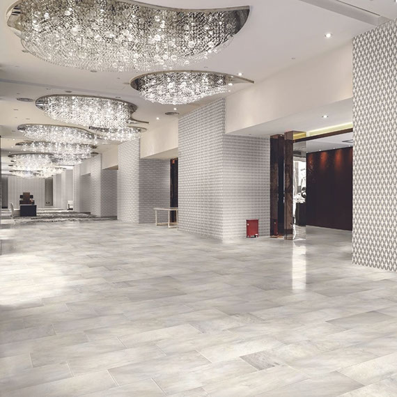 Hotel lobby with white marble floor tile, white & gray marble diamond-shaped mosaic wall tile, and several large crystal chandeliers.