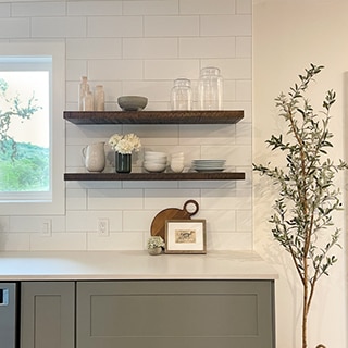 Kitchen backsplash of white subway tile, natural wood floating shelves, white quartz countertops, and gray lower cabinets.