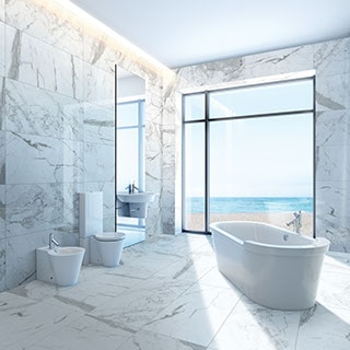 Clean-lined, open bathroom with large windows with an ocean view, soaking tub, and marble-look porcelain large-format tile on the floor and walls.