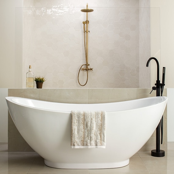 White free-standing soaker bathtub with black faucet in front of open shower, beige floor tile and beige hexagon shower wall tile that looks like stone.