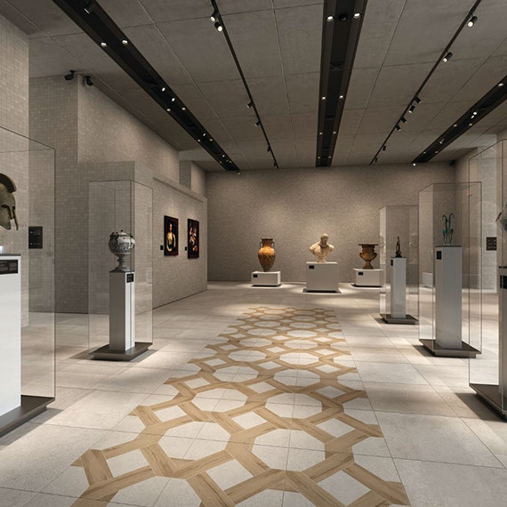 Art museum with concrete-look tan floor tile with inserts that look like wood, paintings on beige mosaic walls, and sculptures on pedestals in glass cases.