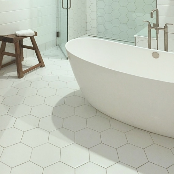Bathroom with white hexagon floor tile, white bathtub, white hexagon shower tile, and a small brown stool. 