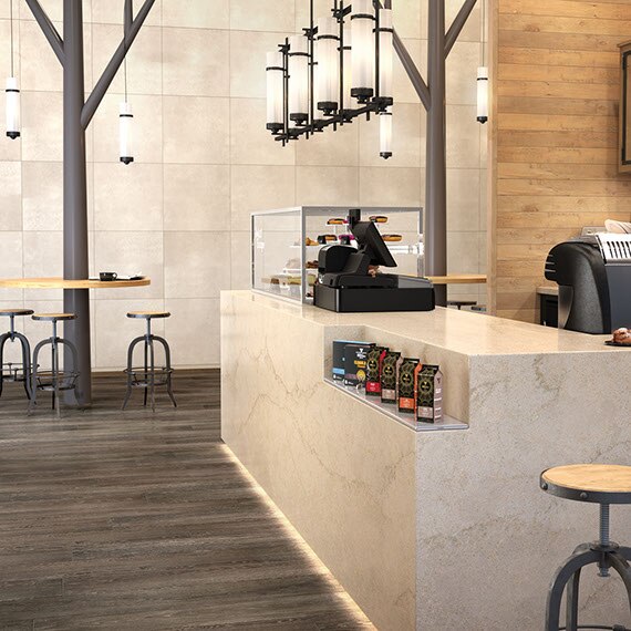 Office building café with tan marble-look quartz countertop with under-counter lighting, black metal & frosted glass pendant lighting, and wooden table & bar stools.