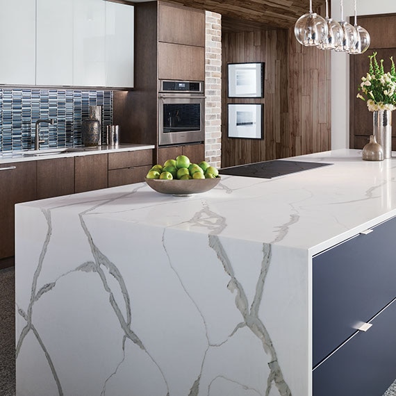 Modern kitchen with marble look, waterfall countertop island, blue glass mosaic tile backsplash, and clear pendant lighting.