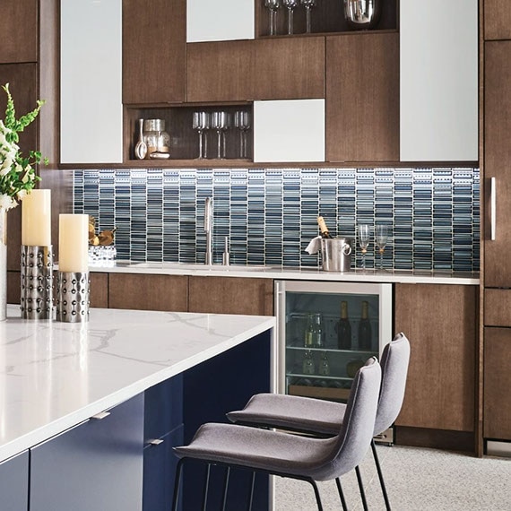 Modern kitchen with marble look, waterfall countertop island, blue glass mosaic tile backsplash, clear pendant lighting, and gray terrazzo floor tile.