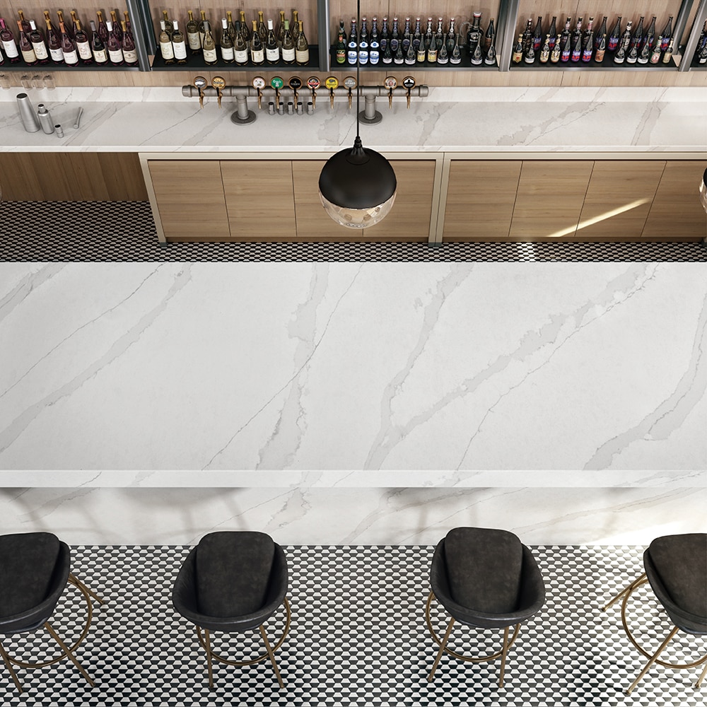 Bar with white marble countertops, light wood cabinets, and wine bottles on back wall.