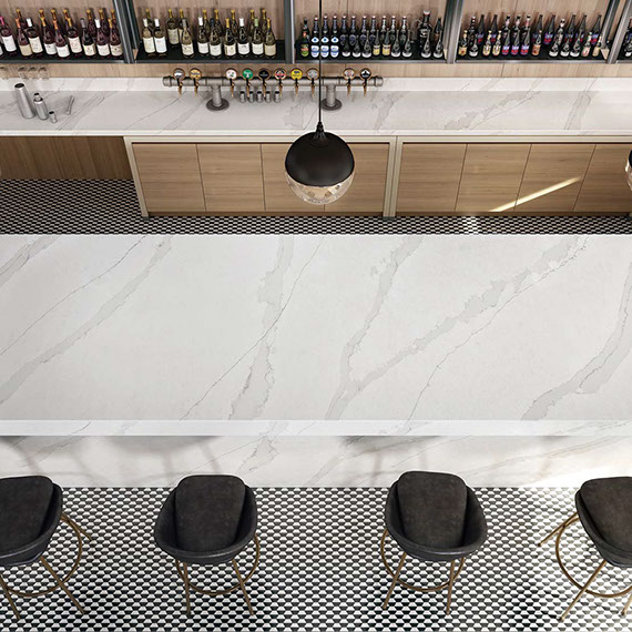 Restaurant bar with white & gray veining quartz countertop, black & white ½ hexagon mosaic floor tile, and black leather & brass bar stools.