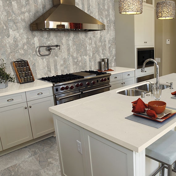 Elegant kitchen features picket marble backsplash behind stainless stain gas stove & hood, and marble floor tile, quartz countertops & island.