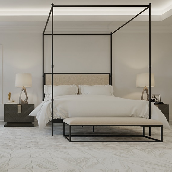 Bedroom with floor tile that looks like white marble with beige and gray veining, black rod iron canopy bed, and two nightstands with lamps.