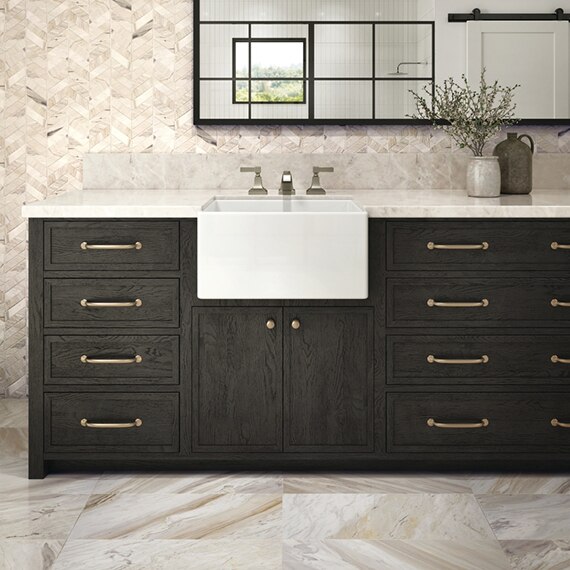 Modern farmhouse bathroom with beige marble chevron mosaic backsplash, farm sink, deep brown cabinets, tan & gray marble tile flooring.