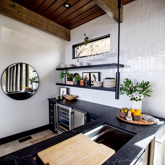 Chip Wade’s residential renovation, Pinhoti Peak, open kitchen with marble-look black quartz countertop, white glossy tile backsplash, and floating shelves.