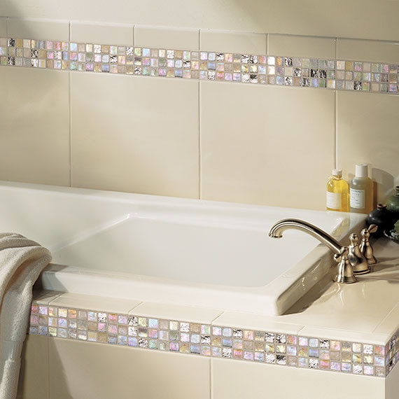 Close up of a bathroom tub and tile surround with twelve inch white tile and iridescent one inch mosaic horzontal stripe accent.