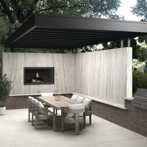 Outdoor patio with pergola, privacy walls and fireplace with natural quartzite slab, wooden table with chairs, grill, and white stone look pavers.