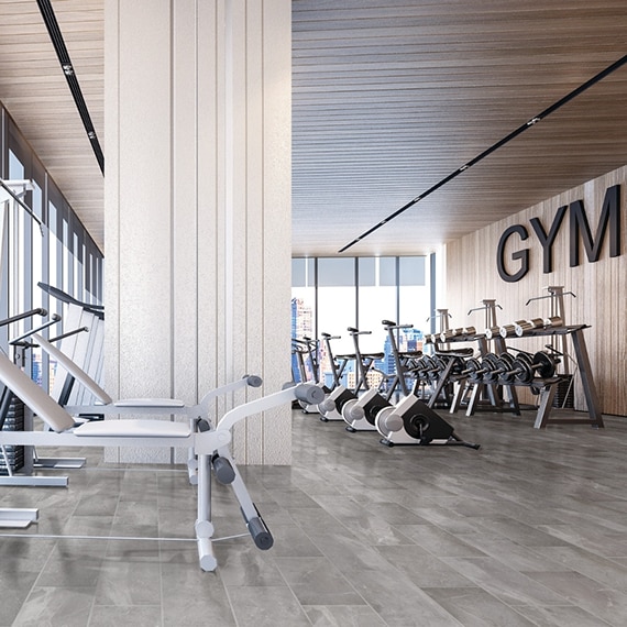 Gym with weight machines, free weights on racks, 12x24 gray marble look floor tile, and floor-to-ceiling windows with view of city skyline.
