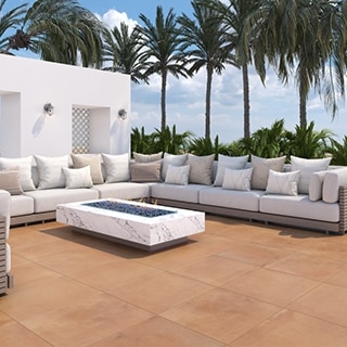 Tropical resort lounge area with terracotta stone look paver flooring, palm trees behind a white sectional sofa that is surrounding a white marble look porcelain firepit.