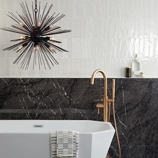 Modern bathroom with soaker bathtub, brushed brass faucet, sunburst chandelier in front of white high-gloss wall tile and black extra-large format porcelain wainscoting.