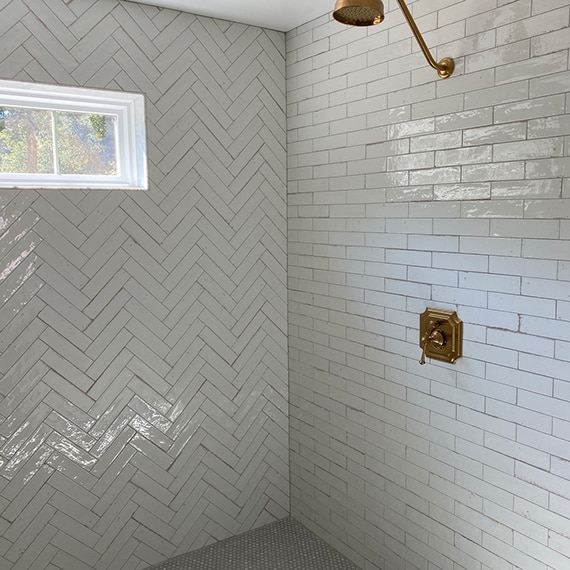 Newly renovated shower with gray penny round shower floor tile, white shower wall tile in a subway pattern and herringbone pattern.