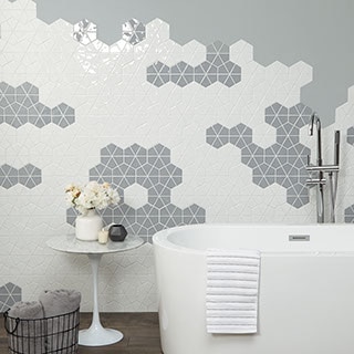 Bathroom feature wall with gray and white six-inch mosaic. Each hexagon is cut into wedges. Soaker tub in the foreground.