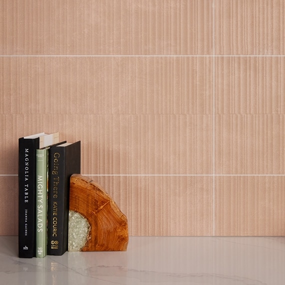 Closeup of textured peach-colored wall tile, curved wood bookend on a white & gray quartz countertop that looks like marble.