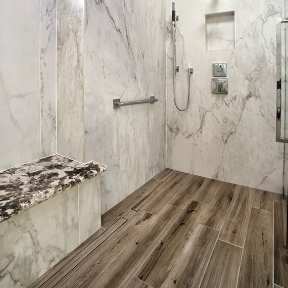 Walk-in shower with walls of off-white & brown porcelain slab that looks like marble and shower floor of wood-look tile.