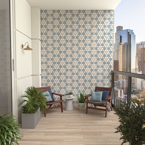 Highrise patio with wood look tile flooring, feature wall with blue & beige decorative wall tile, several potted plants, and wicker chairs around a small table.