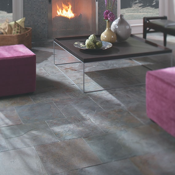Natural slate 24 by 24 inch tile floors in a living room with lavender sofa, glass-top coffee table, and fire in a fireplace.