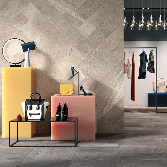 Dress shop with feature wall of beige stone-look tile in a herringbone pattern, dark gray stone-look floor tile, shoes & accessories on yellow & pink blocks.