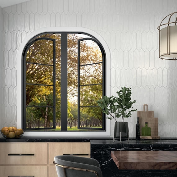 Kitchen with picture window behind black & white marble look porcelain slab countertop & island, glossy white picket wall tile, and natural wood lower cabinets.