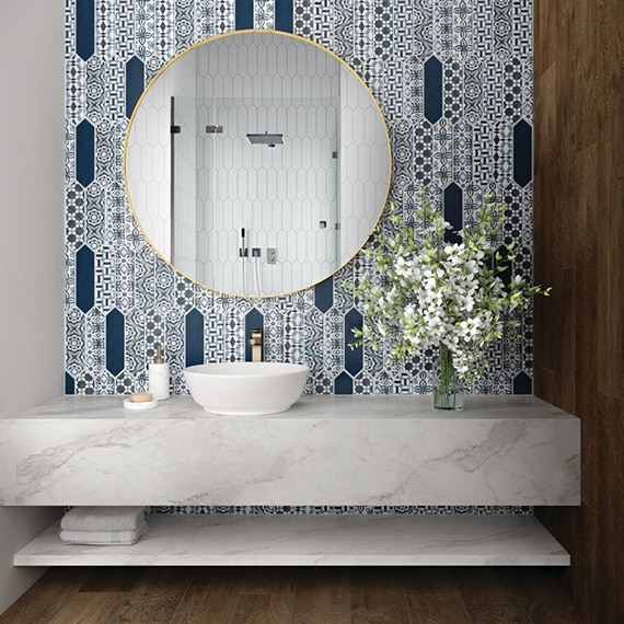 Bathroom vanity with gray marble look countertop of porcelain slab, blue & white encaustic picket tile backsplash, above counter sink, and round mirror.