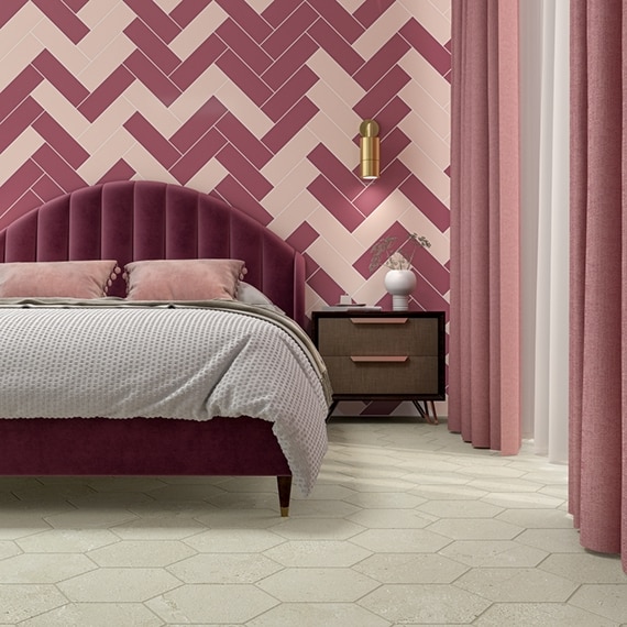 Bedroom with dark and light pink wall tile in a herringbone pattern, dark pink tufted headboard, light pink pillows and curtails, gray comforter, and beige hexagon floor tile.