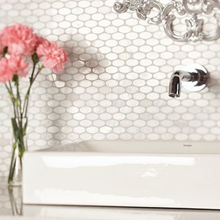 White marble, one-inch oval mosaic on bathroom backsplash with white sink and vase of pink flowers.