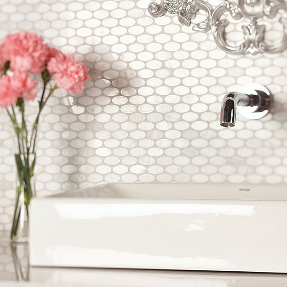 White marble, one-inch oval mosaic on bathroom backsplash with white sink and vase of pink flowers.