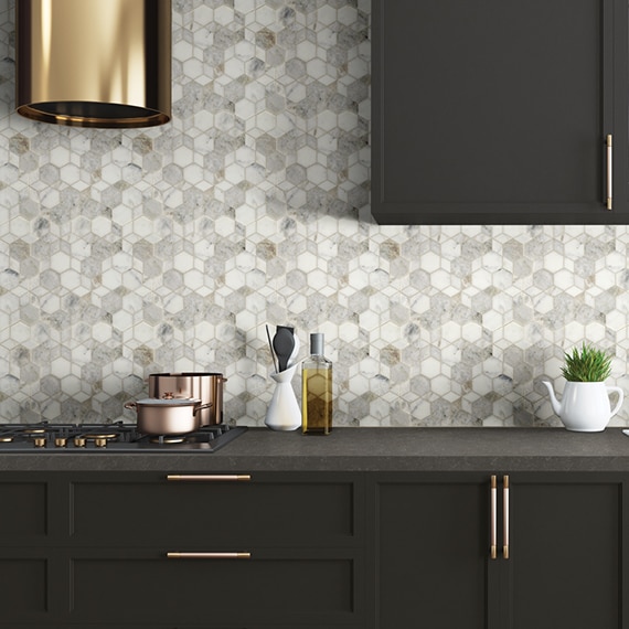 Kitchen white & gray marble mosaic backsplash with brass vent hood over black & brass gas stove, dark brown quartz countertop and cabinets.