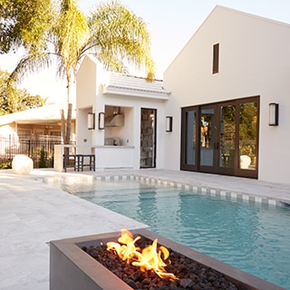 Backyard of white stucco house with outdoor kitchen, firepit, pool with white  & gray waterline tile and white stone look tile deck.