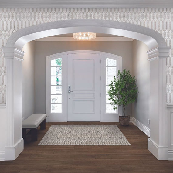 Traditional style home foyer with white and gray marble mosaic wall tile, floor tile that looks like dark wood planks, white front door with side windows.