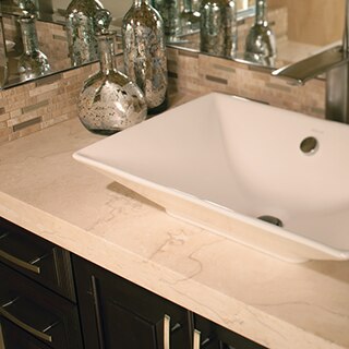 Closeup of tan travertine bathroom vanity with white vessel sink, antique silver glass vases, dark wood cabinets with silver drawer pulls.