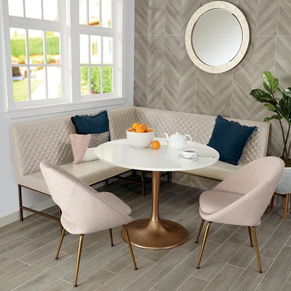 Banquette with beige bench & chairs, table with copper base, chevron pattern wood look backsplash, and wood look tile floor.