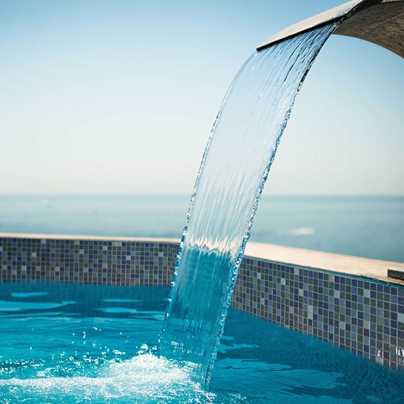 Variegated color, one-inch square mosaic on waterline in fountain with water coming from a spout above.