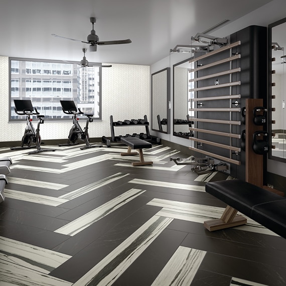 Gym with black floor tile mixed with white & black tile in a herringbone pattern, white chevron wall tile, cycling machine, free weights, and tall mirrors.